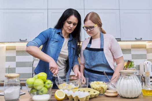 Mother and teenage daughter cooking at home in kitchen. Mom and girl making apple pie together, talking smiling. Relationships, communication parent teenager, healthy homemade food, family concept