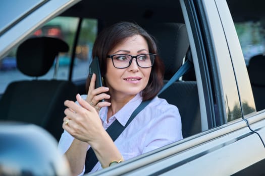 Confident female driver with smartphone driving a car. Serious beautiful female in glasses, lifestyle, transportation, people 40s age concept
