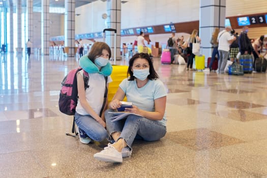 Mother and daughter child in protective medical masks at the airport with luggage suitcases. Tourism, travel, journey, transportation, passenger, vacation, trip concept