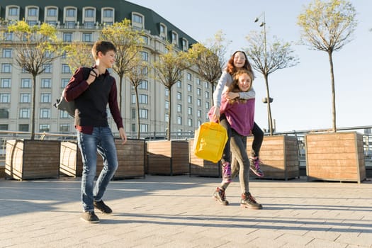 Friends teenagers students with school backpacks, having fun on the way from school. City background, golden hour