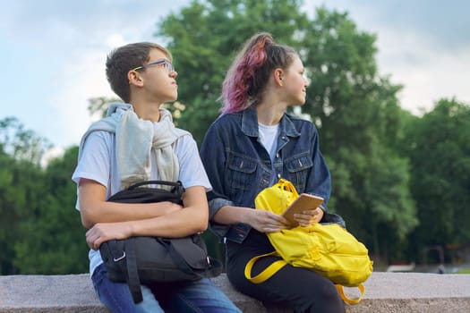Outdoor portrait of two talking teenagers school students, boy and girl students with smartphone