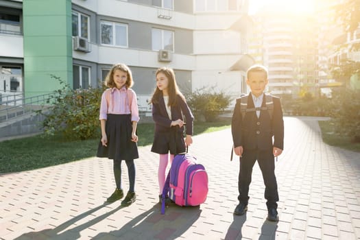 Outdoor portrait of smiling schoolchildren in elementary school. Group of kids with backpacks are having fun, talking. Education, friendship, technology and people concept