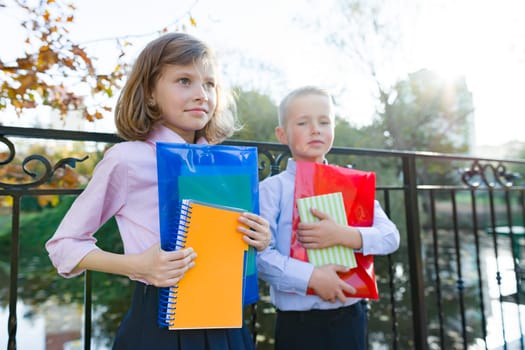 Back to school, portrait of two little school kids. Children boy and girl smile, hold school supplies, background sunny autumn park, golden hour