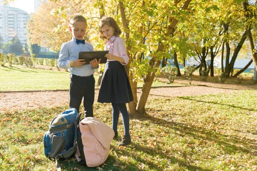 Two kids watching digital tablet, background autumn sunny park, golden hour