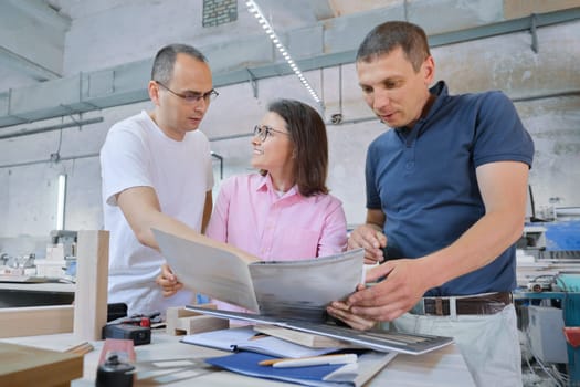 Group of working people discussing work process, wood products in carpentry workshop.