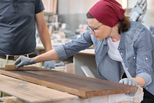 Middle-aged craftswoman working in woodworking workshop. Female varnishing wooden board with oil, varnish. Furniture joinery wood business.