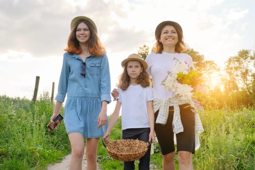 Mother with children two daughters walking along a country road, background summer meadow sunset