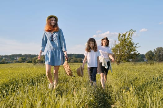 Mother with children two daughters walking along a country road, background summer meadow sunset