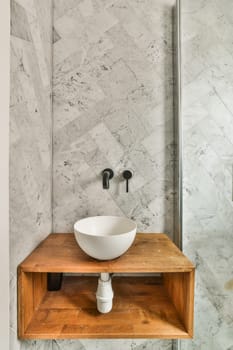 a bathroom with marble walls and flooring, including a vessel bowl sink on a wooden shelf in the corner