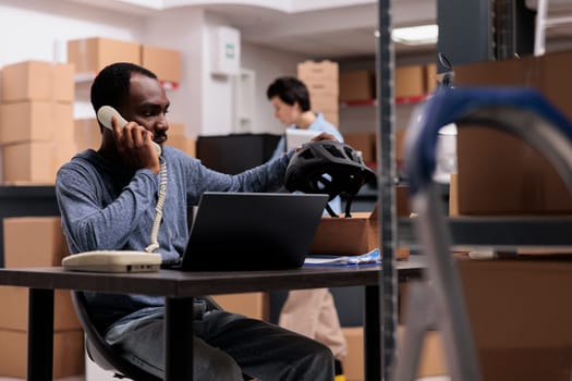 Warehouse supervisor talking at landline phone discussing transportation problem with remote manager while preparing customer packages, putting order in carton box. Concept of storehouse job