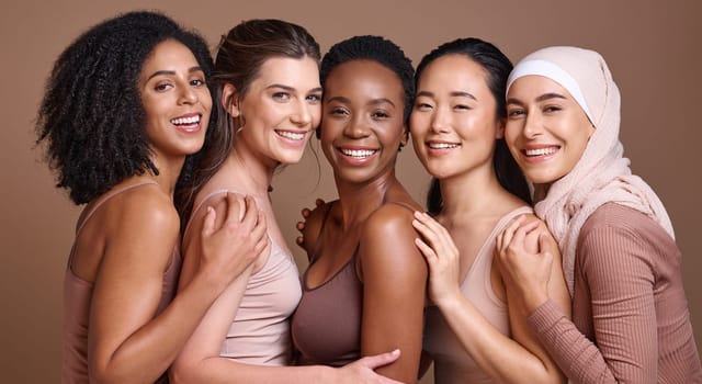 Skincare, diversity and women hug portrait for inclusivity, happiness and healthy skin texture. Interracial beauty and model group with woman in hijab smile for cosmetic campaign in brown studio.