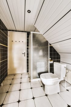 a bathroom with black and white tiles on the walls, floor, and toilet in an attic - style room