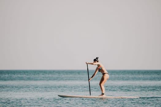 Sea woman sup. Silhouette of happy middle aged woman in rainbow bikini, surfing on SUP board, confident paddling through water surface. Idyllic sunset. Active lifestyle at sea or river