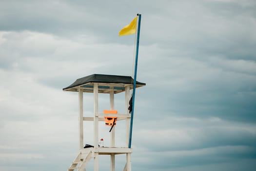 Empty white lifeguard tower with a yellow flag on the beach in windy weather. Beach lifeguard tower with yellow flag indicator. Nobody. Holiday recreation concept