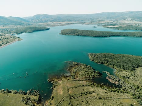 Aerial landscape from flying drone storage reservoir at mountain foot covered colorful spring forest. Beautiful view from above blue lake among highlands