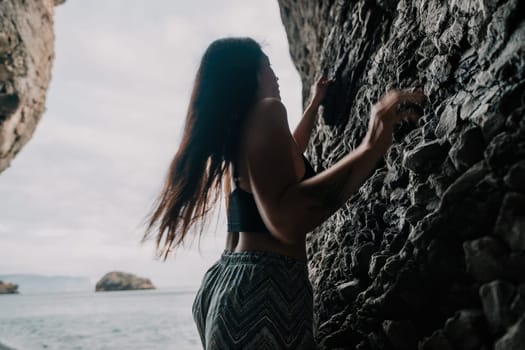 A girl climbs a rock. The athlete trains in nature. Woman overcomes difficult climbing route. Extreme hobby. Tourist woman rock climber hiking on mountains rocks over beautiful sea coast