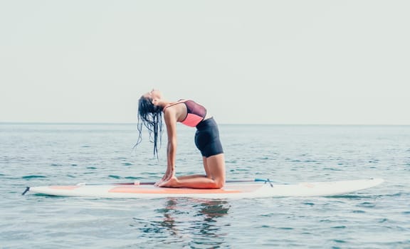 Woman sup yoga. Happy young sporty woman practising yoga pilates on paddle sup surfboard. Female stretching doing workout on sea water. Modern individual female outdoor summer sport activity