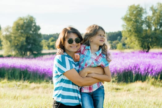 Smiling mother with her little daughter embracing walking on nature, background sunny summer day purple lavender field.