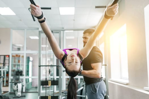 Kinesis technology, kinesitherapy, healthy lifestyle. Young woman doing rehabilitation exercises with personal instructor using kinesi machine, fitness gym background.