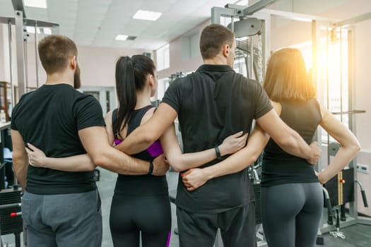 Group of young sports people embracing together in fitness gym backs. Fitness, sport, teamwork, motivation, people, healthy lifestyle concept.