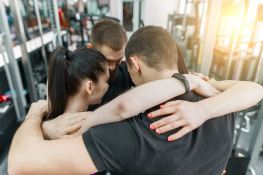 Group of young sports people embracing together in fitness gym backs. Fitness, sport, teamwork, motivation, people, healthy lifestyle concept.