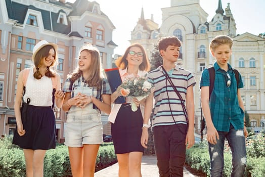 Outdoor portrait of school teacher with bouquet of flowers and group of teenage school children. Children congratulate their teacher, teacher's day