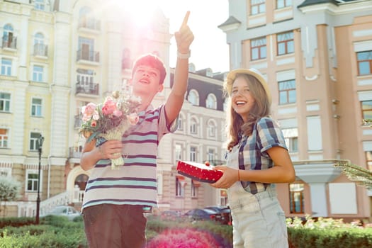 Happy smiling teenagers outdoor, boy holding bouquet of flowers and girl with gift in box.