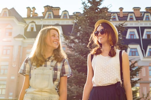 Portrait of two smiling beautiful girls, teenagers 13, 14 years old, close-up, girls talking laughing and walking in summer city
