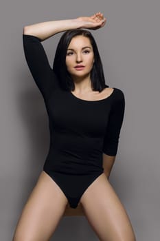 Beauty fashion portrait of young beautiful woman in black bodysuit with long sleeves. Gray studio background, perfect makeup, healthy hair, athletic body