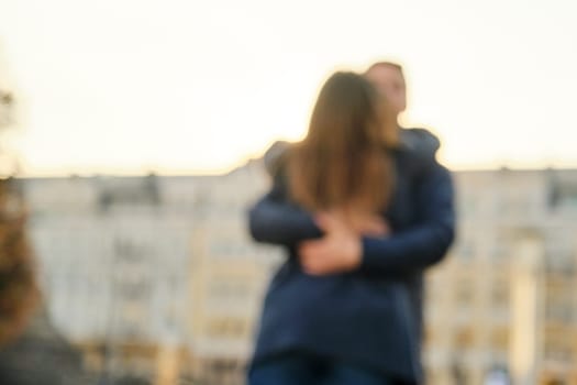 Young man and woman hugging kissing, couple blurred and soft focus, background city, golden hour.