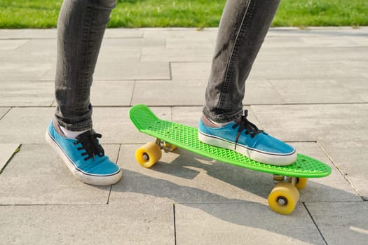 Little girl rides a skateboard, in area near the house, spring season, gray wall background.