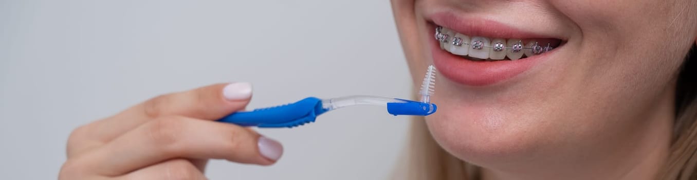 Caucasian woman cleaning her teeth with braces using a brush. Widescreen