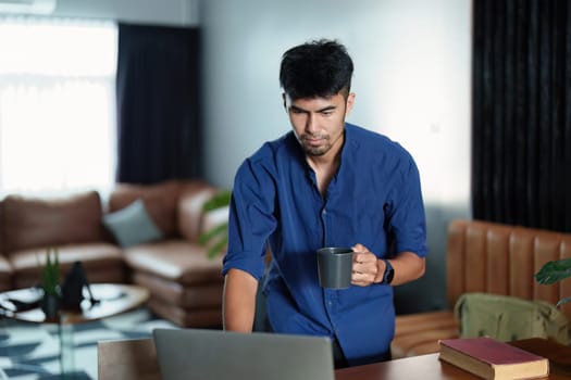 Portrait of an Asian man working on a computer and drinking coffee.