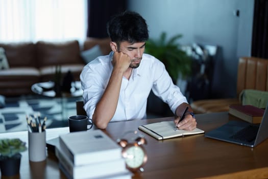 Portrait of an Asian man using a computer and note book to record his work.