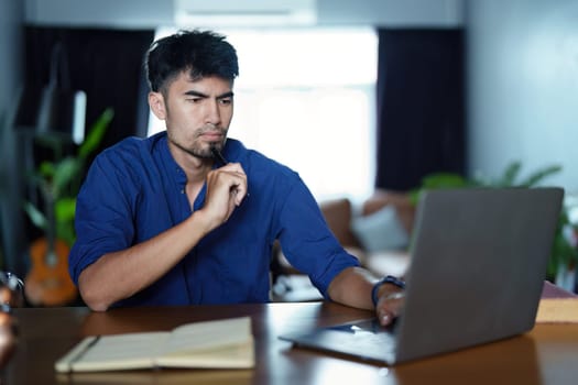 Portrait of an Asian man using a computer and note book to record his work.