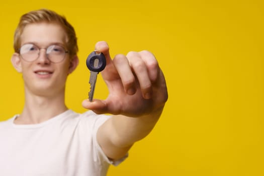Cheerful young man with glasses holding the key to a property or apartment against a bright yellow background. Perfect copy space for real estate or property-related designs. High quality photo
