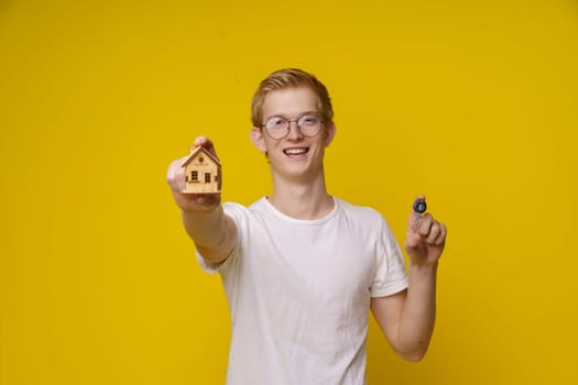 Young man holds a model of a house and a key, symbolizing his independence and entry into the housing market. This image represents the concept of affordable real estate for the youth and the importance of financial planning and property ownership. High quality photo