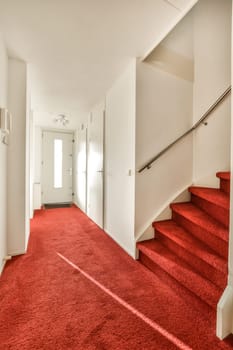a red carpet in a white room with stairs leading up to the second floor and an open door on the right side
