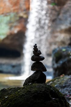 Silhouetted cairn stacked stones with blurry background of waterfall.