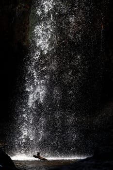 Splashing waterfall drop on pond with dark background of cave in summer.