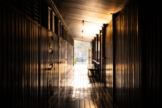 Dark hallway inside wooden residence building with bright sunlight at the end.