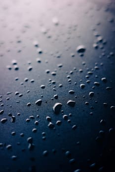 Selective focus on water drops on slippy surface of black synthetic fabric with bright light from background.