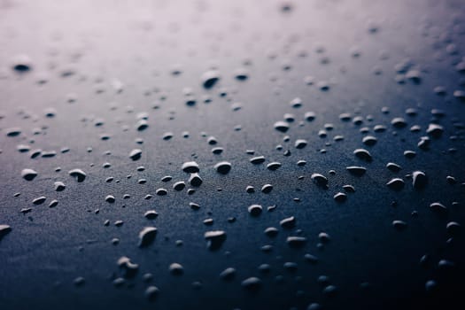 Selective focus on water drops on slippy surface of black synthetic fabric with bright light from background.