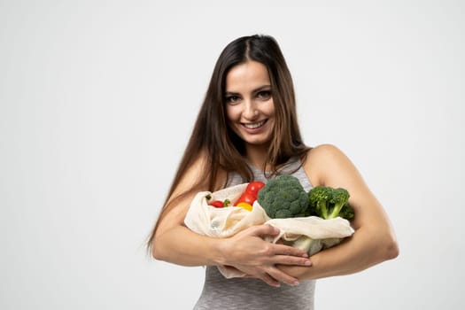 Smiling brunette girl is holding mesh shopping bag with vegetables, greens without plastic bags. Zero waste, plastic free Eco friendly concept. Sustainable lifestyle