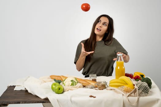 Happy woman in green t-shirt unpacking shopping mesh eco bag with healthy vegetables, fruits, bread, snacks on the kitchen at home. Healthy eating vegetarian concept