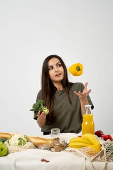 Happy woman in green t-shirt unpacking shopping mesh eco bag with healthy vegetables, fruits, bread, snacks on the kitchen at home. Healthy eating vegetarian concept