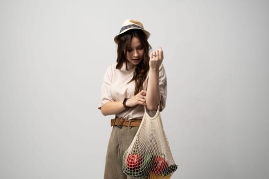 Zero waste concept. A young girl holds on her hand a textile mesh eco bag with a groceries. The girl smiles, wearing a beige t-shirt and hat. Refusal of plastic bags