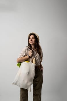 Zero waste concept. Young brunette woman holding mesh eco bag with organic fruits and vegetables. Using reusable crochet net bag for grocery shopping