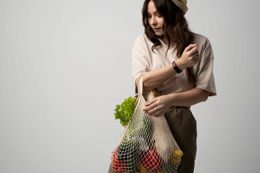 Brunette women in dress holds mesh bag with vegetables, fruits and groceries. Concept of no plastic. Zero waste, plastic free. Eco friendly concept. Sustainable lifestyle