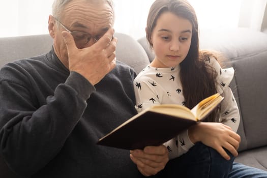 Happy little girl with grandfather reading story book at home.